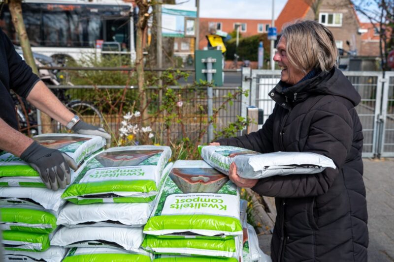 een vrouw staat lachend met een zak compost in haar handen